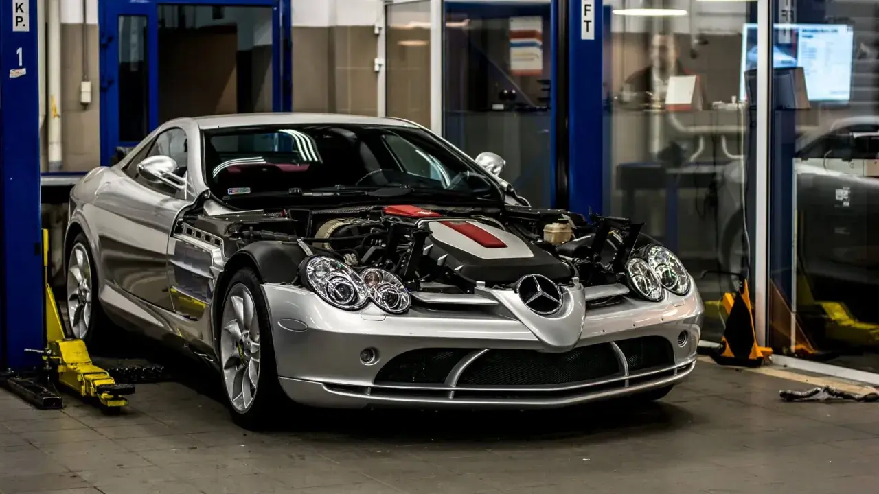 Srebrny Mercedes McLaren z otwartą maską, odsłaniającą potężny silnik, stoi w warsztacie.