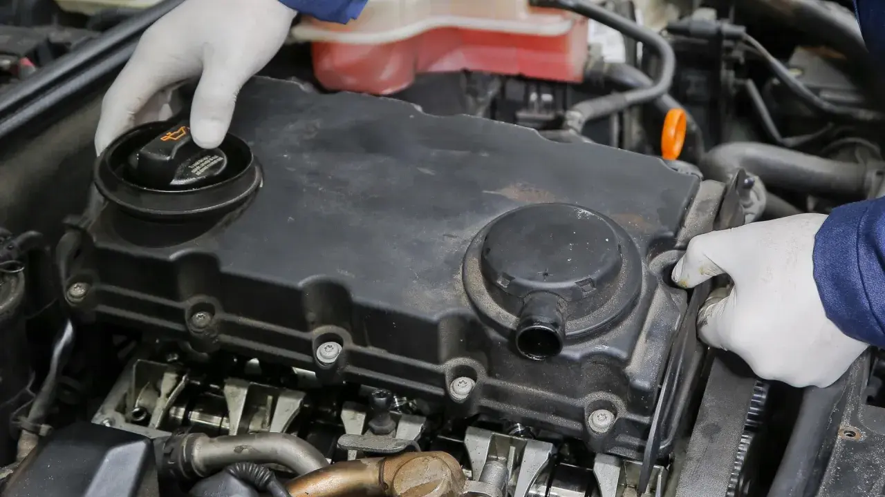Mechanik w białych rękawiczkach sprawdza silnik, odkręcając korek wlewu oleju. Widoczne elementy silnika i układu odmy.