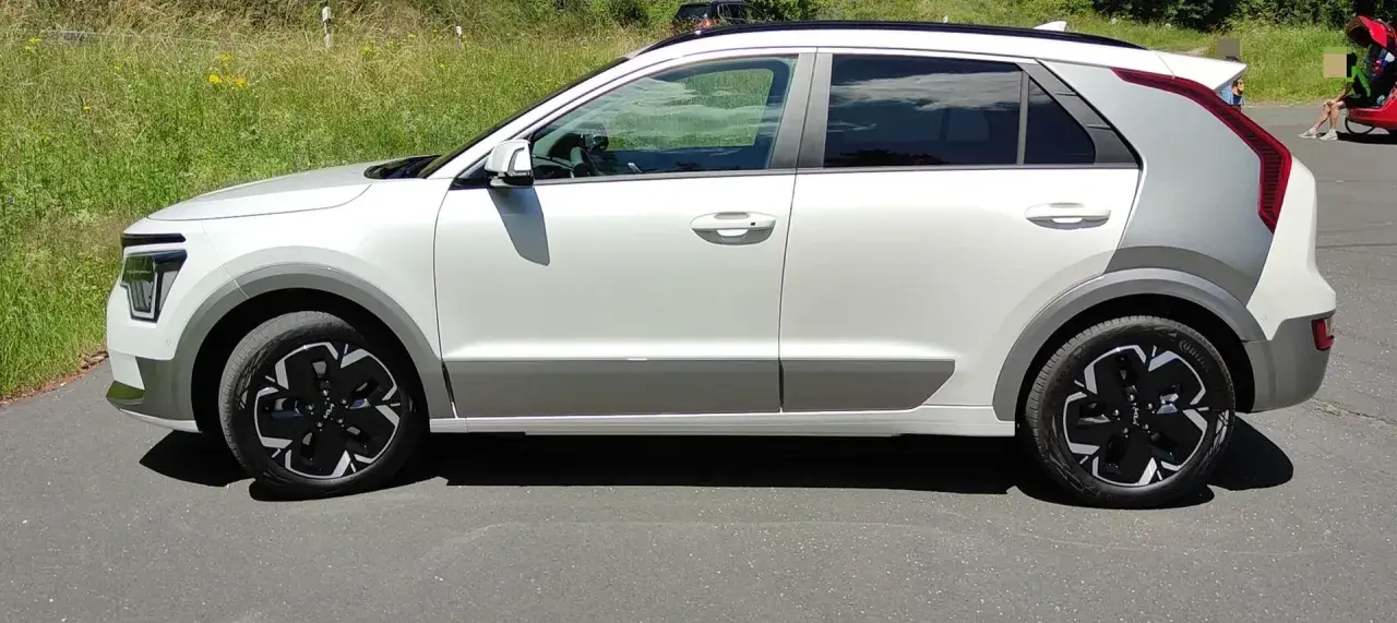 Biały Kia Niro EV z czarnymi felgami stoi na drodze, otoczony zielenią.
