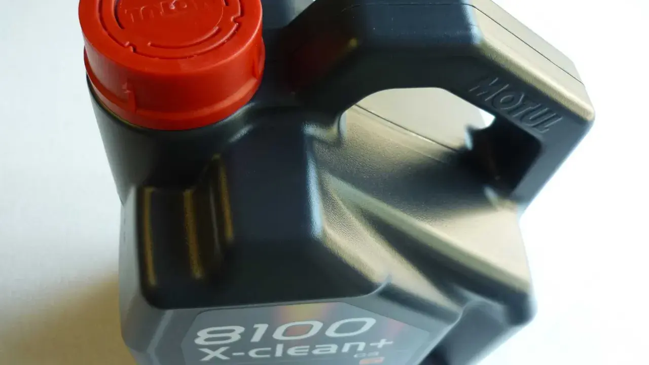 Czarny kanister z olejem silnikowym Motul 8100 X-clean+ z czerwoną zakrętką.
