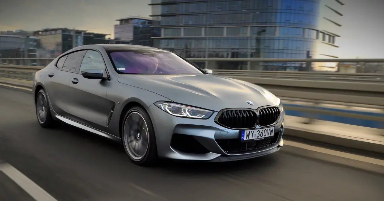 Srebrne BMW M850i sunie po moście, odbijając światła miasta w swoich szybach.