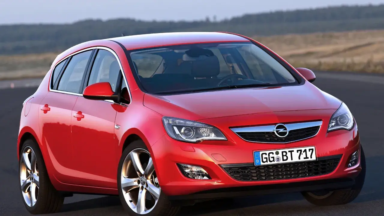 Czerwony Opel Astra 4 na drodze, z widokiem na wzgórza w tle.