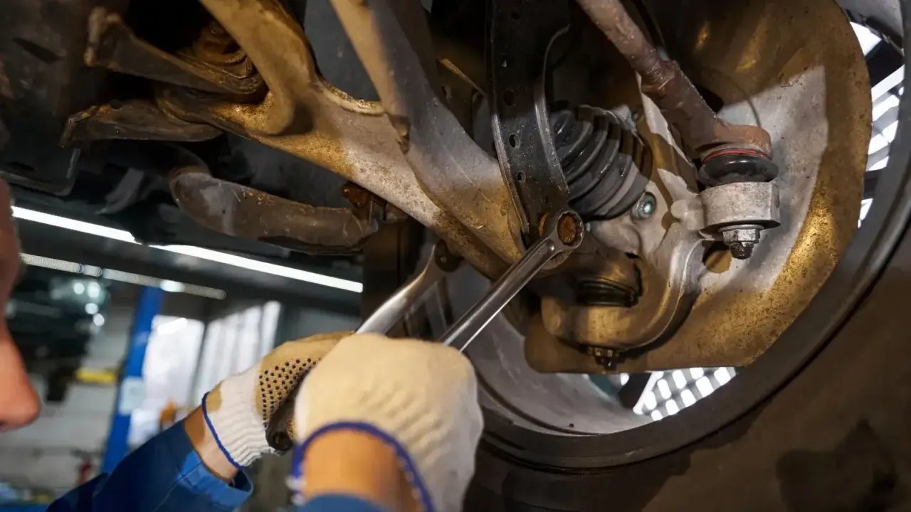 Mechanik dokręca śrubę w zawieszeniu samochodu kluczem.