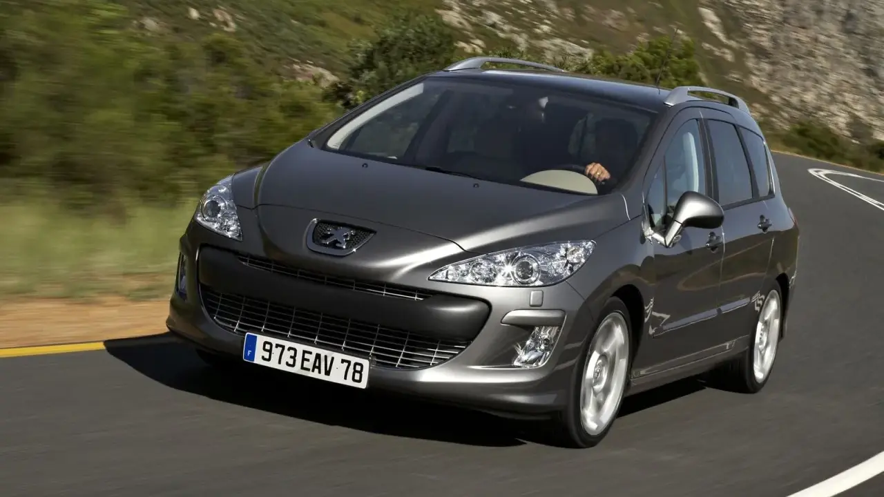 Szary Peugeot 308 2008 na krętej drodze wśród zielonych wzgórz.