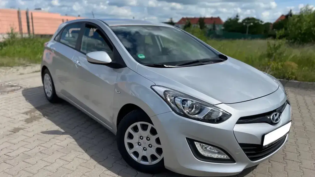 Srebrny Hyundai i30 1.4 benzyna zaparkowany na kostce brukowej, w tle zielona trawa i budynki.