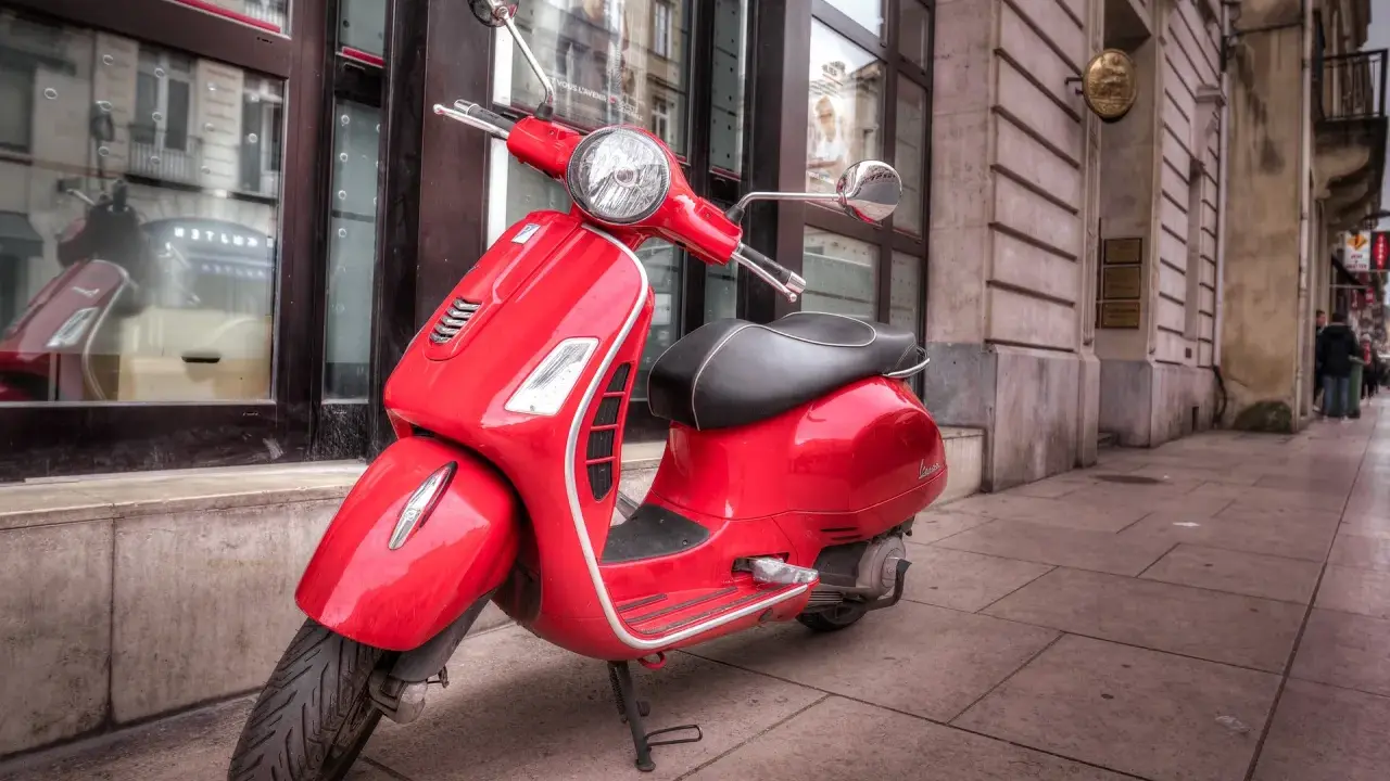Czerwona Vespa na chodniku. Czy można nią jeździć mając prawo jazdy AM od ilu lat?