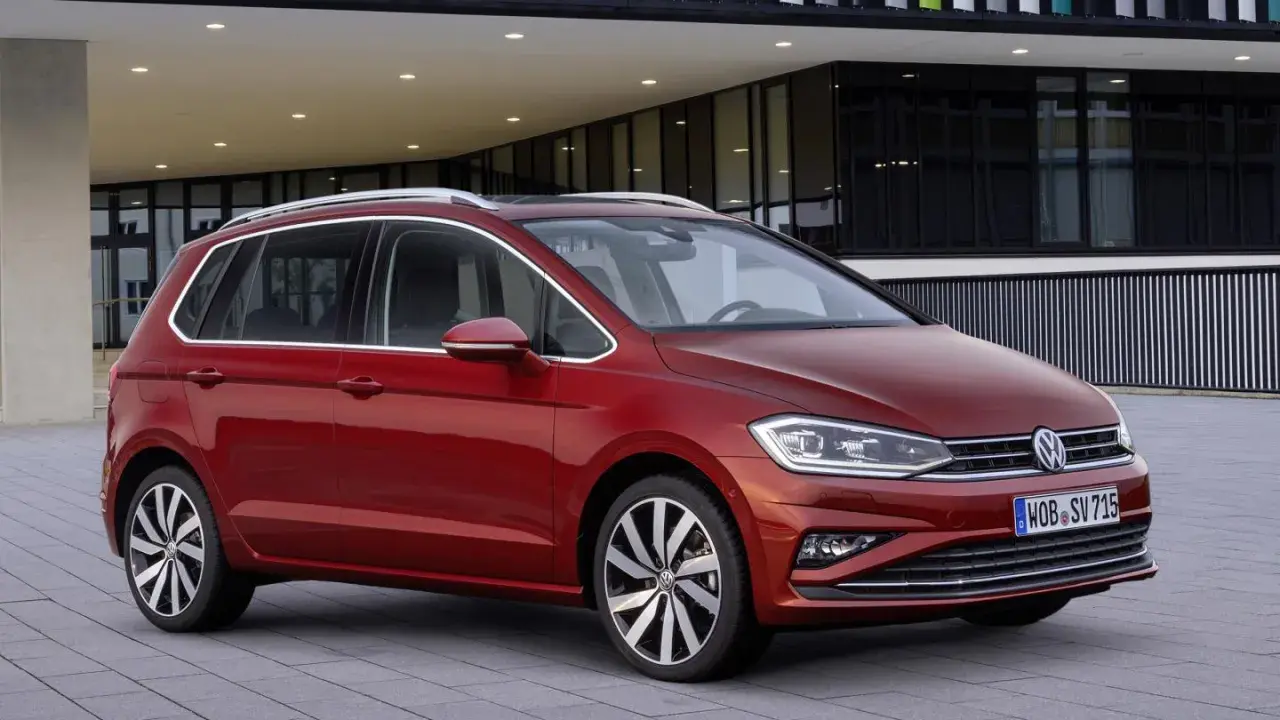 Czerwony Volkswagen Golf Sportsvan przed nowoczesnym budynkiem. Wady tego modelu mogą dotyczyć np. wyciszenia kabiny.