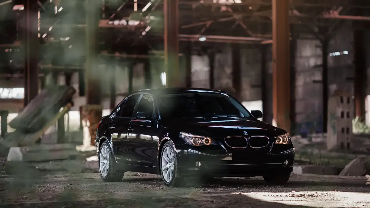 Czarny BMW 535d w opuszczonej hali, otoczony mgłą i gruzem.