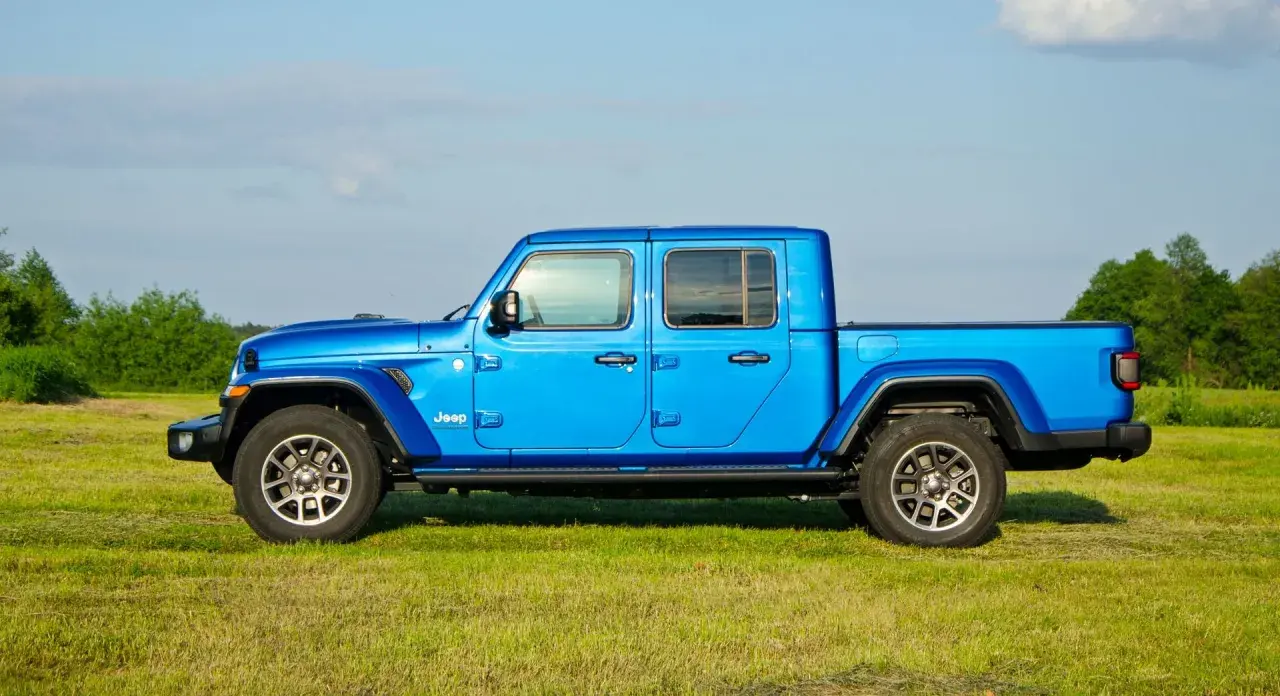 Niebieski Jeep Gladiator na tle zielonej łąki i drzew. Ten wszechstronny pickup jest gotowy na każdą przygodę.