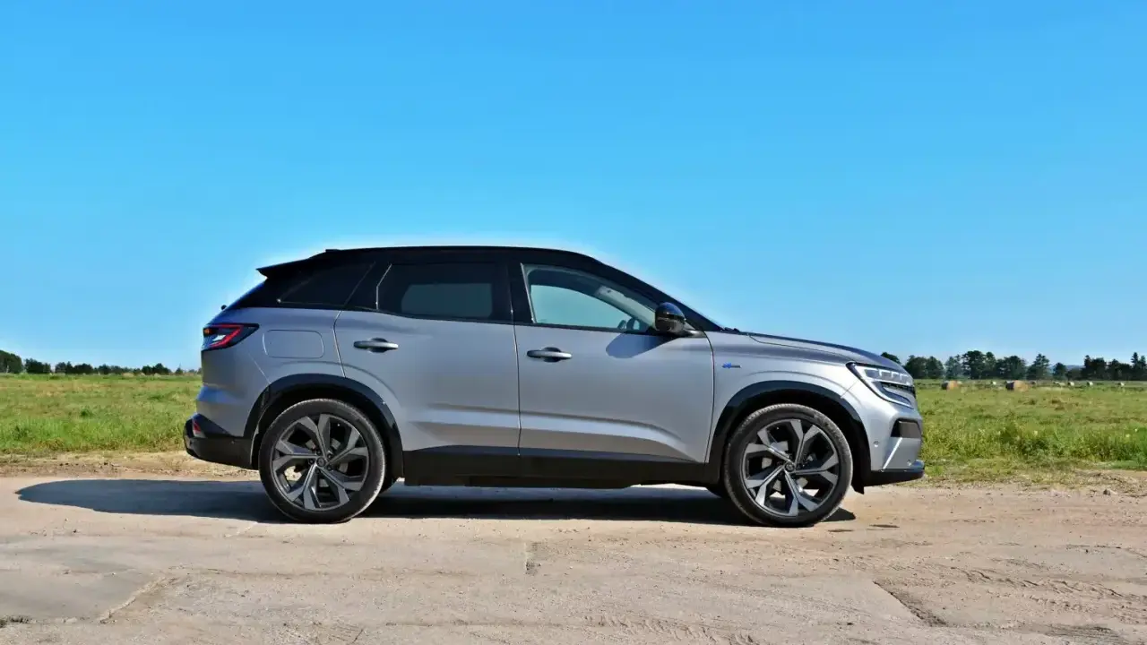 Nowy Renault Austral w kolorze srebrnym, zaparkowany na polnej drodze, z zielonym polem i niebieskim niebem w tle.