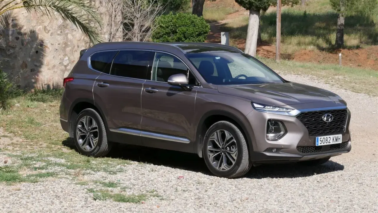 Brązowy Hyundai Santa Fe 2025 na tle kamiennego muru i zieleni.