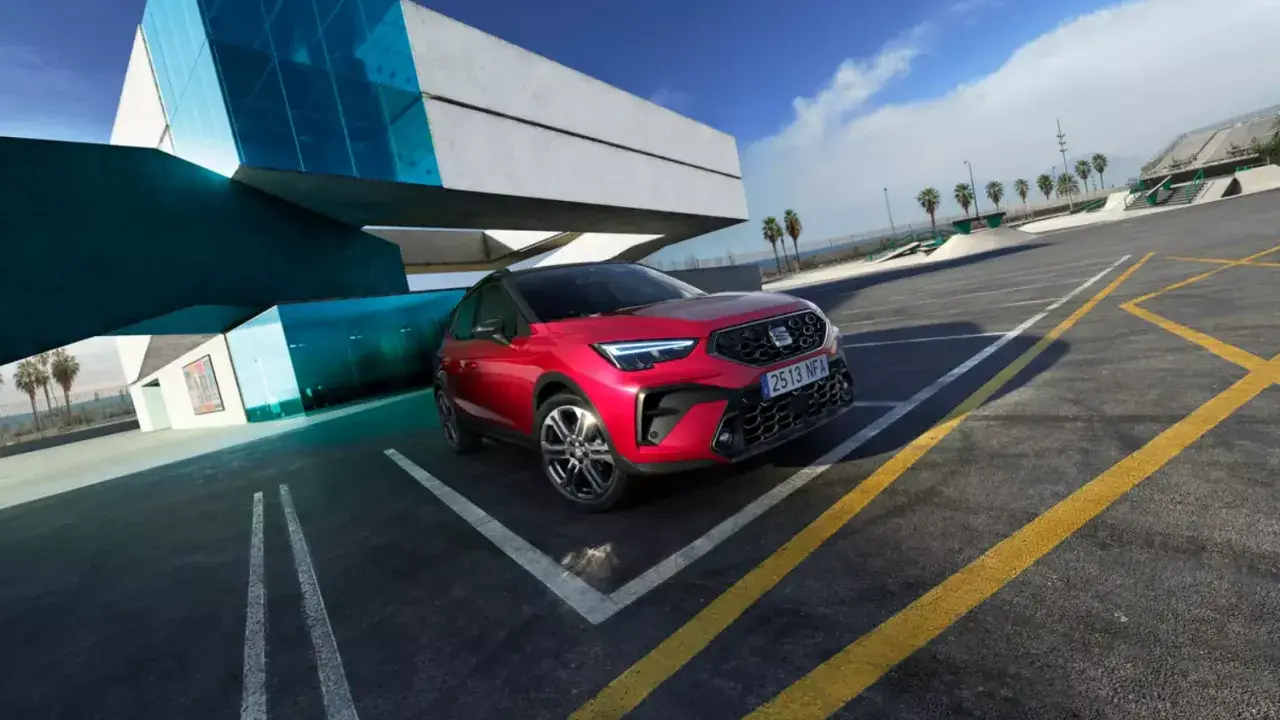 Czerwony Seat Arona, jeden z najnowszych seat modele, zaparkowany przy nowoczesnym budynku z niebieskimi akcentami.