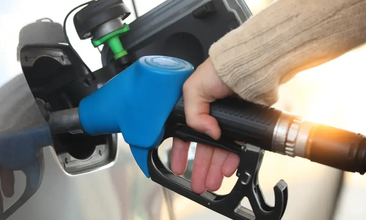 Dłoń trzymająca niebieski pistolet do tankowania paliwa przy samochodzie.