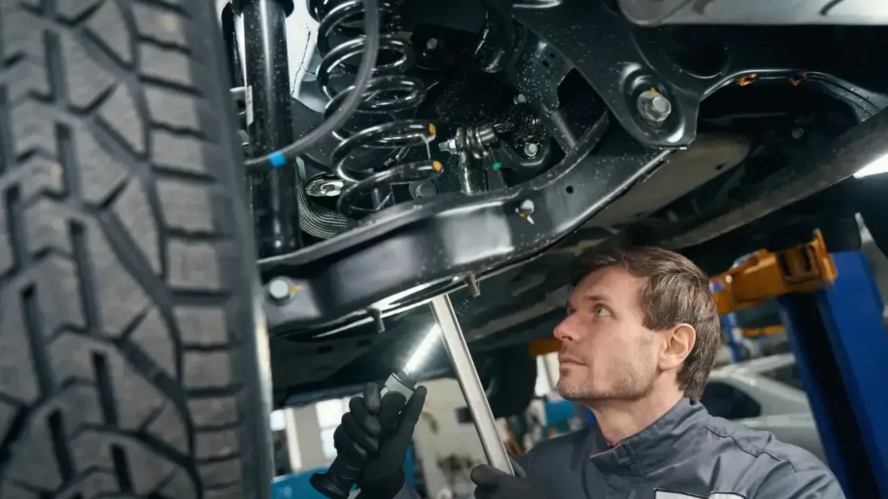 Mechanik bada podwozie samochodu, oświetlając latarką skomplikowany wielowahacz i sprężynę amortyzatora.