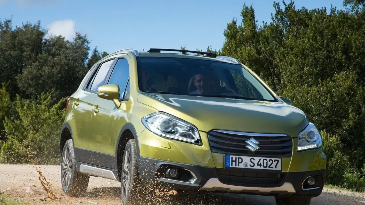Zielony Suzuki SX4 S-Cross pokonuje teren, wzbijając kurz. Mimo że auto radzi sobie na bezdrożach, warto rozważyć jego wady przed zakupem.