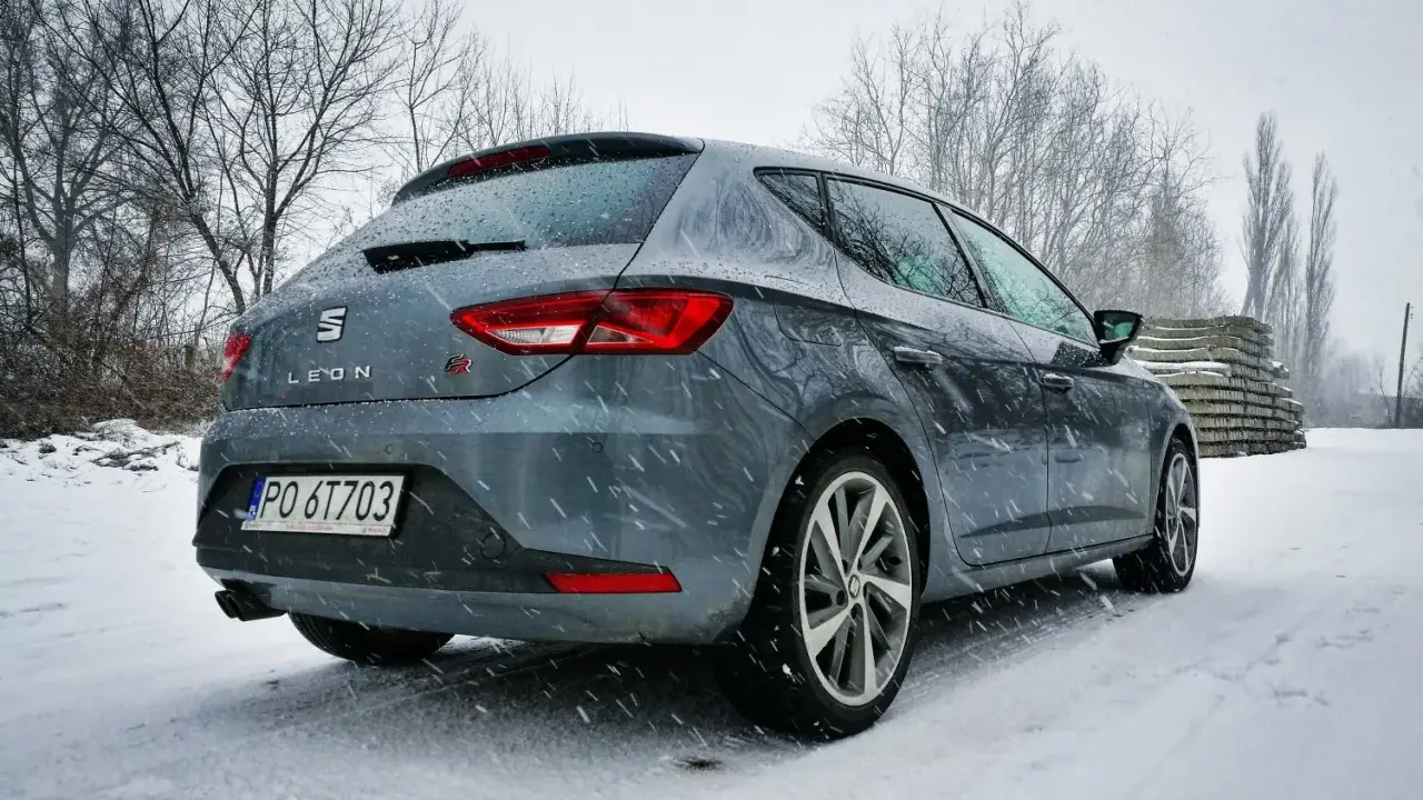 Szary Seat Leon FR w zimowej scenerii, pokryty śniegiem.