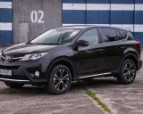 Czarny, używany Toyota RAV4 z salonu, zaparkowany przed budynkiem z niebiesko-białymi pasami.