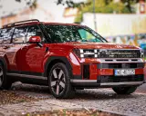 Czerwony Hyundai Santa Fe z nowoczesnym designem stoi na brukowanej drodze, otoczony jesiennymi liśćmi.