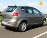 Szary Seat Altea XL jedzie autostradą. W tle widać żółty autobus i znak ostrzegawczy.