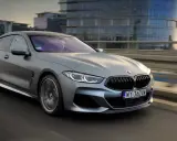 Srebrne BMW M850i sunie po moście, odbijając światła miasta w swoich szybach.