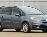 Szary Citroen Picasso z napisem "Picasso" na błotniku, zaparkowany przed budynkiem.