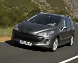 Szary Peugeot 308 2008 na krętej drodze wśród zielonych wzgórz.