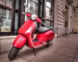 Czerwona Vespa na chodniku. Czy można nią jeździć mając prawo jazdy AM od ilu lat?