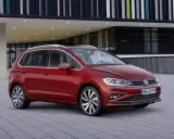 Czerwony Volkswagen Golf Sportsvan przed nowoczesnym budynkiem. Wady tego modelu mogą dotyczyć np. wyciszenia kabiny.