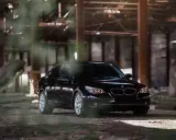 Czarny BMW 535d w opuszczonej hali, otoczony mgłą i gruzem.