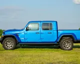 Niebieski Jeep Gladiator na tle zielonej łąki i drzew. Ten wszechstronny pickup jest gotowy na każdą przygodę.
