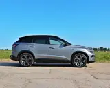 Nowy Renault Austral w kolorze srebrnym, zaparkowany na polnej drodze, z zielonym polem i niebieskim niebem w tle.