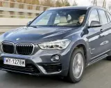 Ciemnoszary BMW X1 2025 z kierowcą za kierownicą, jadący po drodze.