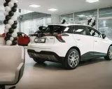 Białe auto MG 4 Electric w salonie, ozdobionym balonami. Obok czerwony samochód i wygodne fotele.