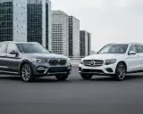 Dwa luksusowe mercedes suv modele, biały i szary, stoją obok siebie na tle nowoczesnych wieżowców.