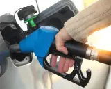 Dłoń trzymająca niebieski pistolet do tankowania paliwa przy samochodzie.