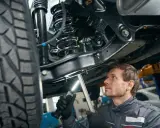 Mechanik bada podwozie samochodu, oświetlając latarką skomplikowany wielowahacz i sprężynę amortyzatora.