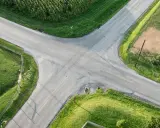 Rozjazd dróg na wsi, gdzie obowiązuje zasada prawej ręki. Wokół pola kukurydzy i zielone łąki.