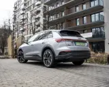 Srebrny Audi Q4 e-tron zaparkowany na brukowanym podjeździe przed nowoczesnym budynkiem mieszkalnym.