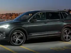 Ciemnozielony SUV, jeden z najbardziej polecanych samochodów 7-osobowych, zaparkowany nocą na parkingu z widokiem na oświetlone budynki.