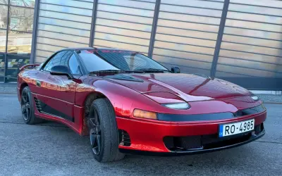 Czerwony Mitsubishi 3000GT z czarnymi felgami i przyciemnianymi szybami, zaparkowany przed nowoczesnym budynkiem.