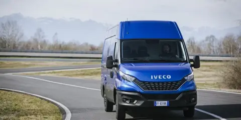 Niebieski Iveco Daily 3 na zakręcie drogi, z kierowcą za kierownicą. W tle góry i drzewa.