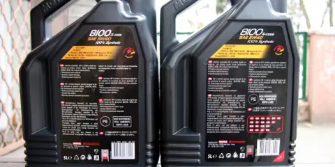 Dwie kanistry oleju silnikowego Motul 8100 X-cess SAE 5W40, jeden oznaczony jako "FAKE", drugi jako "ORI".