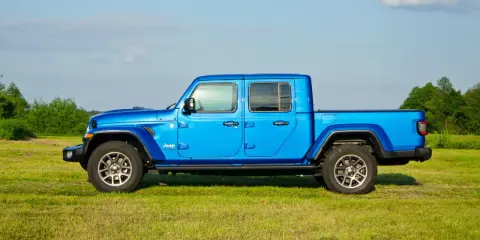 Niebieski Jeep Gladiator na tle zielonej łąki i drzew. Ten wszechstronny pickup jest gotowy na każdą przygodę.