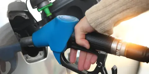 Dłoń trzymająca niebieski pistolet do tankowania paliwa przy samochodzie.