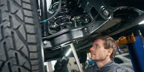 Mechanik bada podwozie samochodu, oświetlając latarką skomplikowany wielowahacz i sprężynę amortyzatora.