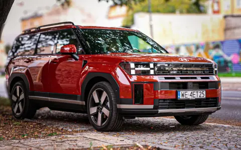 Czerwony Hyundai Santa Fe z nowoczesnym designem stoi na brukowanej drodze, otoczony jesiennymi liśćmi.
