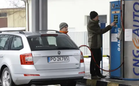 Srebrny samochód Skoda z podłączoną dyszą do tankowania gazu CNG na stacji.