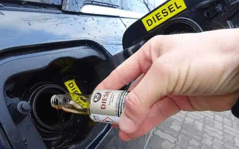 Ręka wlewa dodatek do diesla z małej buteleczki do baku samochodu.