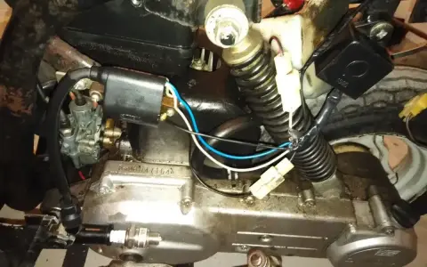 Silnik motoroweru z widocznym iskrownikiem, gaźnikiem i świecą zapłonową.