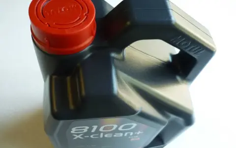 Czarny kanister z olejem silnikowym Motul 8100 X-clean+ z czerwoną zakrętką.